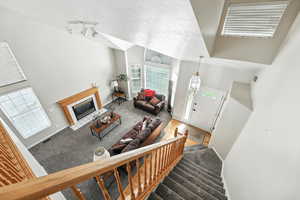 Carpeted foyer featuring a tile fireplace, a high ceiling, a textured ceiling, stairway, and rail lighting