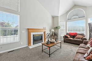 Carpeted living area with a tiled fireplace and high vaulted ceiling