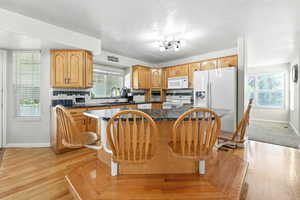 Kitchen featuring white appliances, dark countertops, a kitchen island, light wood-type flooring, and decorative backsplash