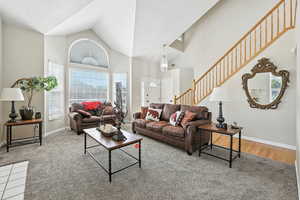 Carpeted living room with high vaulted ceiling and stairway