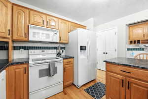 Kitchen with decorative backsplash, white appliances, light wood-type flooring, and brown cabinetry
