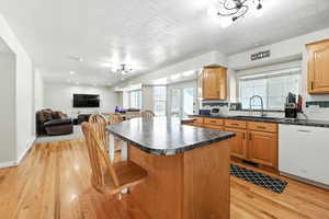 Kitchen featuring dishwasher, light wood-style floors, decorative backsplash, a kitchen bar, and dark countertops