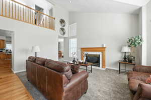 Living area with a tiled fireplace, high vaulted ceiling, plenty of natural light, and carpet floors