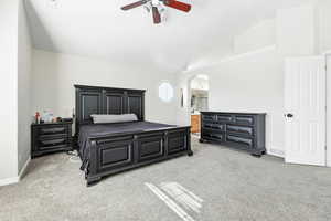 Bedroom with lofted ceiling, carpet floors, ensuite bath, arched walkways, and ceiling fan