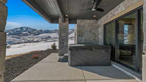 Snow covered patio with a patio area, a ceiling fan, a mountain view, and a hot tub