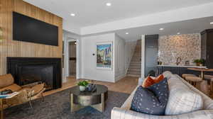 Living room featuring stairs, an accent wall, a large fireplace, light wood finished floors, and recessed lighting