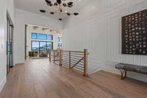 Hallway with an upstairs landing, beamed ceiling, wood finished floors, a chandelier, and a decorative wall