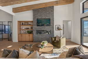 Living room featuring high vaulted ceiling, wood finished floors, a stone fireplace, and beam ceiling