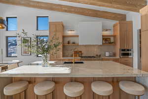 Kitchen with open shelves, decorative backsplash, light stone countertops, and a large island