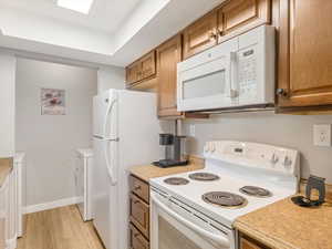Kitchen with white appliances, light countertops, washer / dryer, and light wood-type flooring