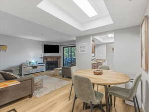 Dining space with a tray ceiling, a stone fireplace, and light wood-style flooring