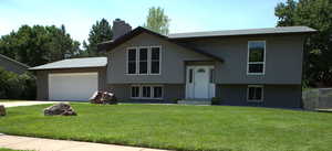 Bi-level home with a chimney, a garage, driveway, and brick siding