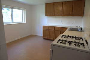 Kitchen with white gas range, brown cabinetry, and light countertops