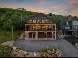 Rustic home featuring stone siding, a balcony, driveway, and a garage