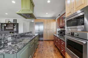 Kitchen featuring appliances with stainless steel finishes, custom range hood, hardwood / wood-style floors, recessed lighting, and dark stone counters