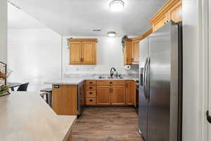 Kitchen with stainless steel refrigerator with ice dispenser, a textured ceiling, a peninsula, light countertops, and dark wood finished floors