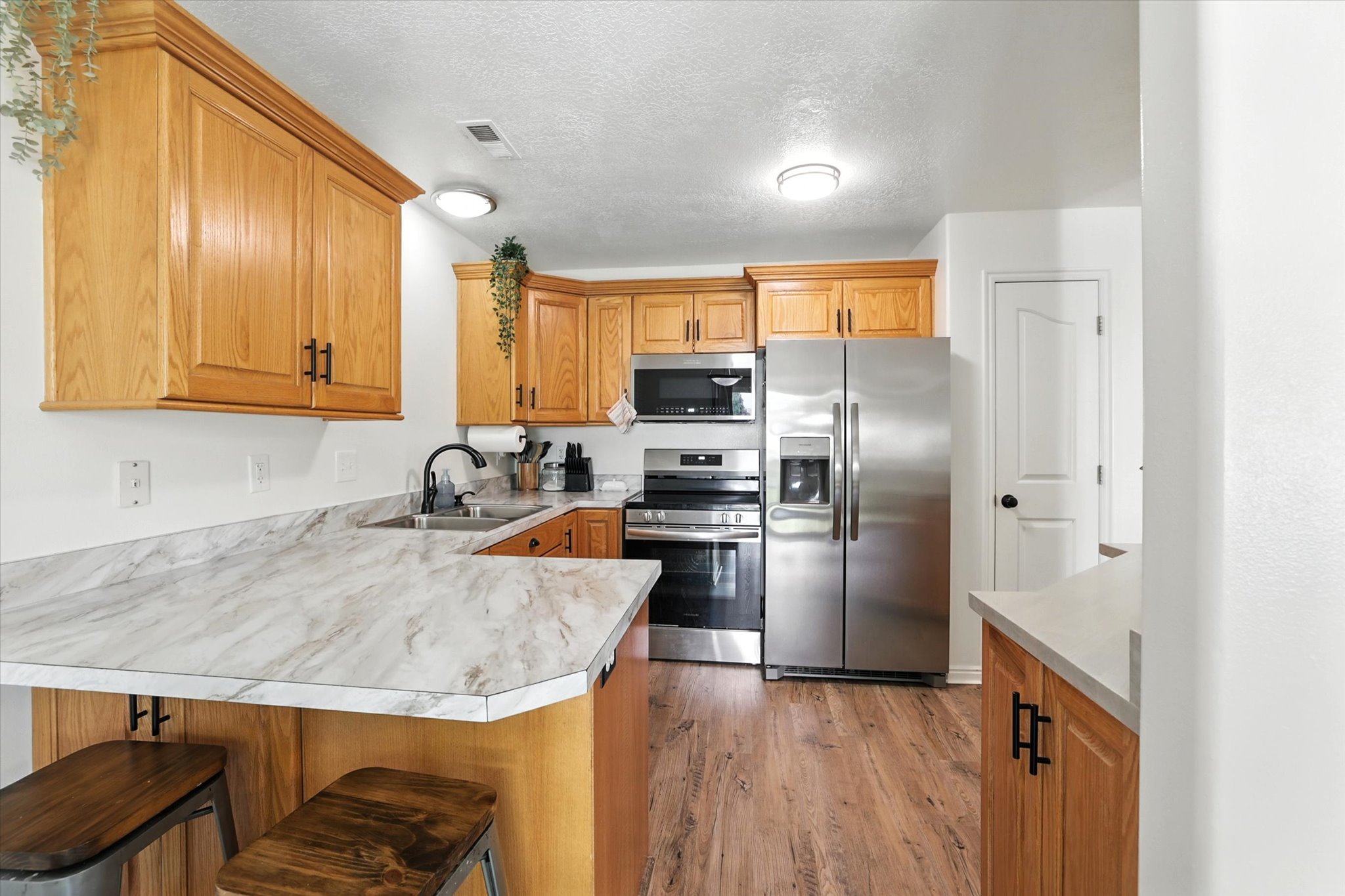 Kitchen featuring stainless steel appliances, light wood finished floors, a peninsula, a kitchen bar, and light countertops