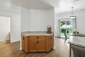 Kitchen featuring a textured ceiling, stainless steel dishwasher, light wood-style floors, pendant lighting, and light countertops