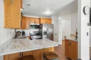 Kitchen featuring appliances with stainless steel finishes, a peninsula, light wood finished floors, a textured ceiling, and light countertops