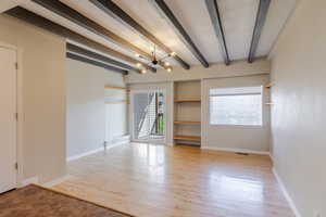 Unfurnished room featuring a chandelier, beamed ceiling, plenty of natural light, and wood-type flooring