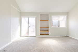 Carpeted spare room featuring lofted ceiling and built in shelves