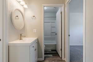 Bathroom with vanity, a textured wall, wood finished floors, and washtub / shower combination