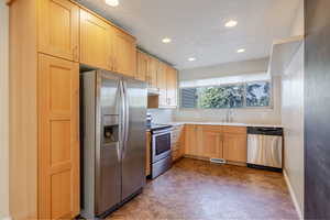 Kitchen with stainless steel appliances, light brown cabinetry, light countertops, recessed lighting, and a textured ceiling