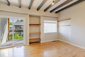 Unfurnished bedroom with access to exterior, wood-type flooring, and beamed ceiling