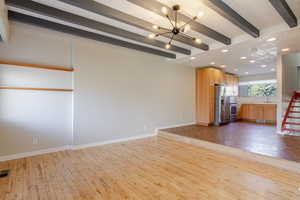 Unfurnished living room with recessed lighting, light wood-type flooring, beam ceiling, a chandelier, and stairs