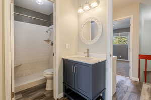 Full bathroom featuring wood finished floors, tiled shower, vanity, a textured ceiling, and a textured wall