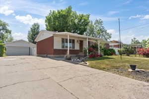 Single story home featuring a porch, a front lawn, an outbuilding, a detached garage, and brick siding