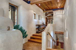 Staircase with a wooden ceiling with exposed beams, concrete flooring, healthy amount of natural light