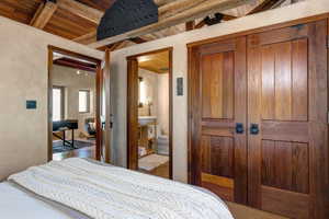 Bedroom featuring a wooden ceiling with exposed beams and connected bathroom