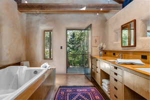 Primary Bathroom with a wood ceiling with exposed beams, double vanity, a bath, and high vaulted ceiling with sandstone countertops and tile