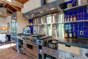 Kitchen featuring wall chimney range hood, high quality appliances, open shelves, backsplash, and sandblasted granite countertops