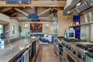 Kitchen with stainless steel countertops, wall chimney exhaust hood, high quality appliances, concrete floors, and wood ceiling