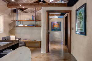 Hallway with finished concrete floors, an office area, and a wooden ceiling with exposed beams