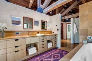 Primary Bathroom with a wood ceiling with exposed beams, double vanity, a bath, and high vaulted ceiling with sandstone countertops and tile
