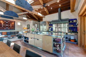 Kitchen with stainless steel counters, a wood ceiling with exposed beams, open shelves, high vaulted ceiling, and stainless steel built in refrigerator
