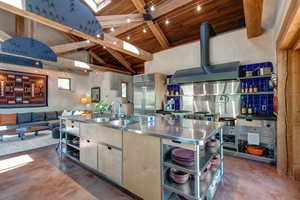 Kitchen with stainless steel countertops, open shelves, a wood ceiling with exposed beams, concrete flooring, and high vaulted ceiling