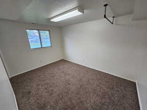 Carpeted empty room featuring a textured ceiling and baseboards