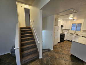 Kitchen featuring white cabinetry, a textured ceiling, white appliances, light stone counters, and dark tile patterned floors