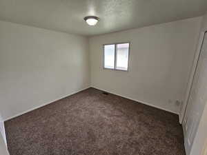 Unfurnished bedroom with a textured ceiling, dark carpet, and a closet