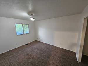 Spare room featuring dark carpet and a textured ceiling