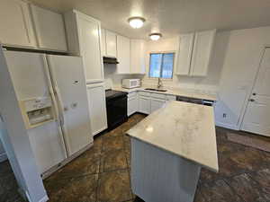 Kitchen with white cabinets, white appliances, a textured ceiling, light stone countertops, and a kitchen island