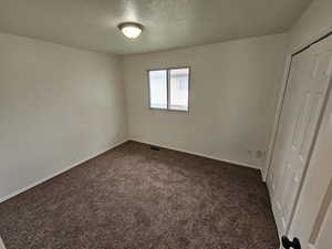 Unfurnished bedroom with a textured ceiling, a closet, and dark carpet