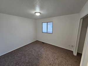 Unfurnished bedroom with dark carpet, a closet, and a textured ceiling