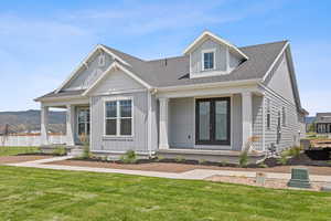 View of front of home with a porch, roof with shingles, a front lawn, and french doors
