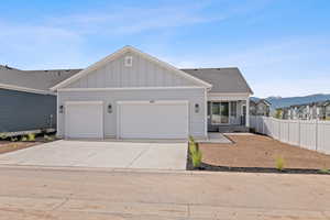 View of back of house featuring board and batten , driveway, a garage, and a shingled roof