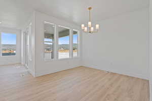 Unfurnished dining area featuring plenty of natural light, light wood-type flooring, a chandelier, and a textured ceiling